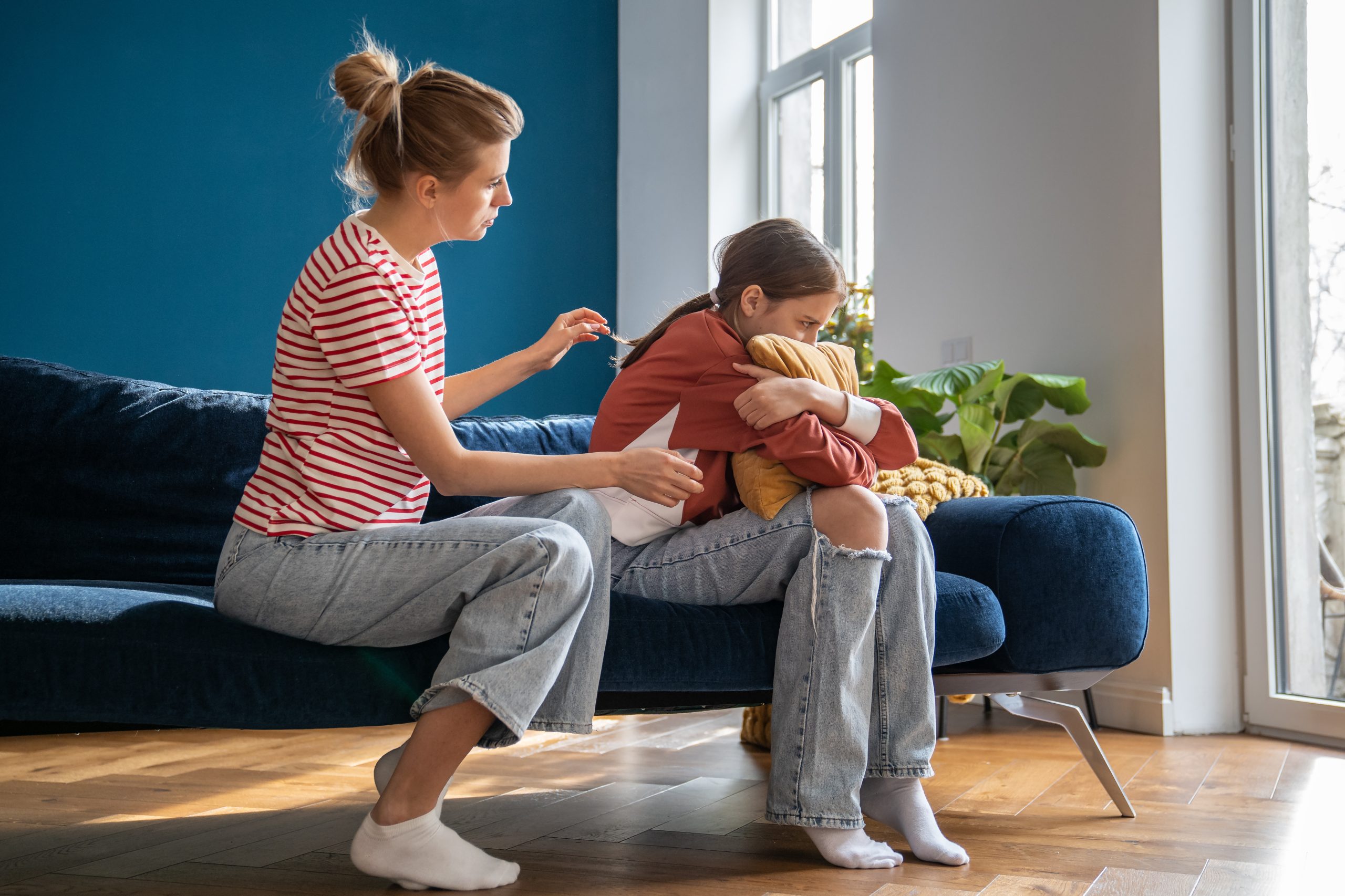 Eine Frau wendet sich einem zurückgezogenen Mädchen mit einem Kissen auf dem Sofa zu